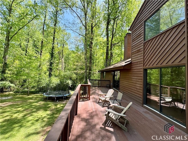 deck featuring a lawn, a view of trees, and a trampoline