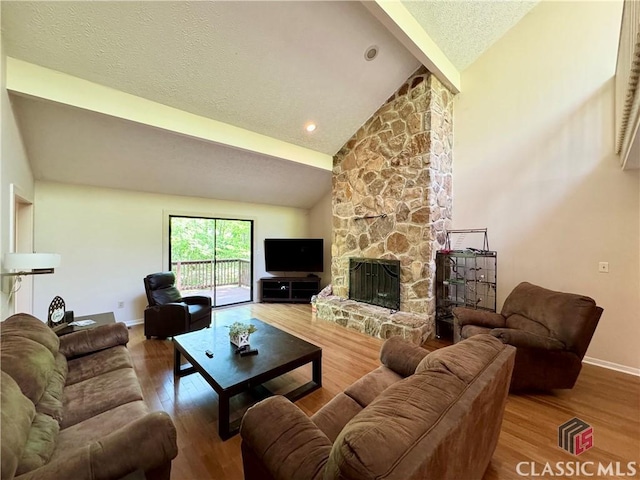 living room featuring wood finished floors, baseboards, lofted ceiling with beams, a fireplace, and a textured ceiling