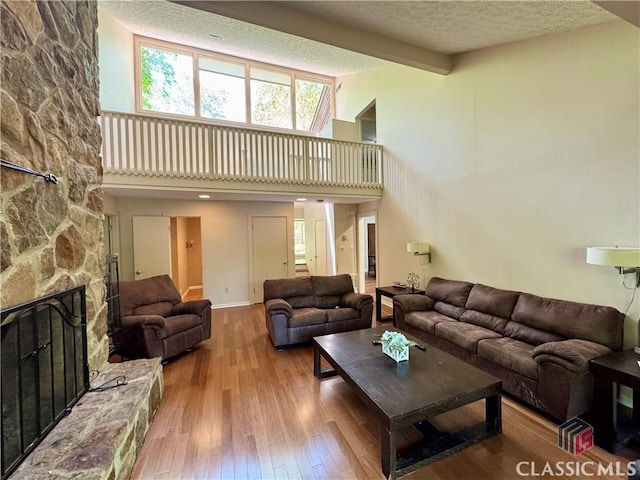 living area featuring wood-type flooring, a textured ceiling, a fireplace, and a towering ceiling