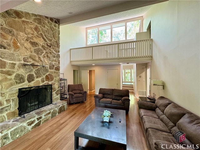living room with a high ceiling, wood finished floors, a stone fireplace, visible vents, and a textured ceiling