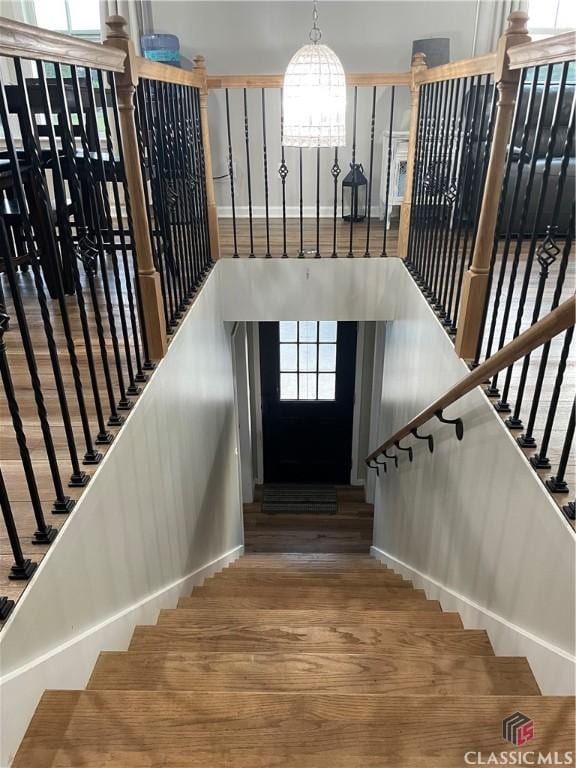 staircase with a notable chandelier, plenty of natural light, and wood finished floors