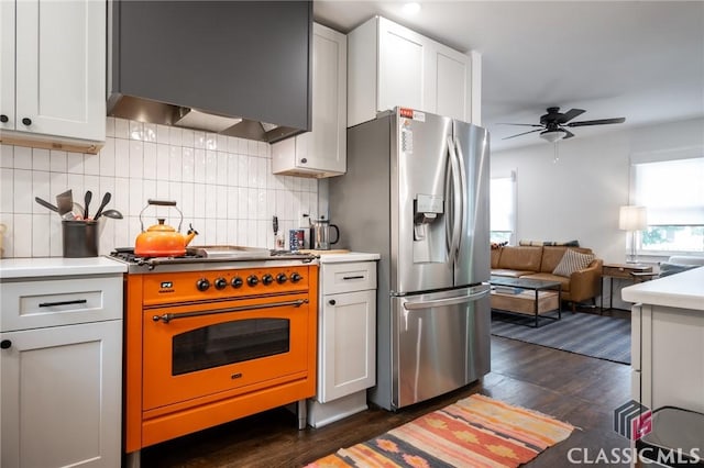 kitchen with wall chimney range hood, backsplash, dark wood-style floors, stainless steel refrigerator with ice dispenser, and range with gas cooktop