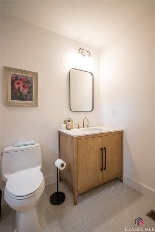 half bathroom with toilet, visible vents, vanity, and baseboards