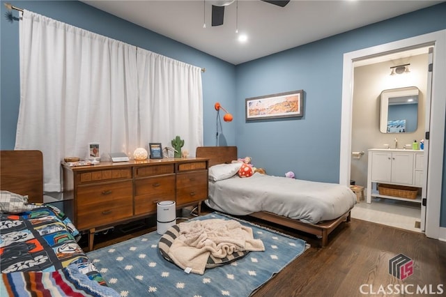 bedroom featuring wood finished floors, ceiling fan, ensuite bath, and a sink