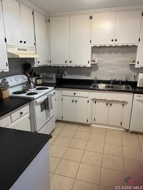 kitchen with light tile patterned floors, a sink, dark countertops, under cabinet range hood, and white appliances