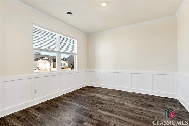 empty room with a decorative wall, a wainscoted wall, visible vents, ornamental molding, and dark wood-style floors