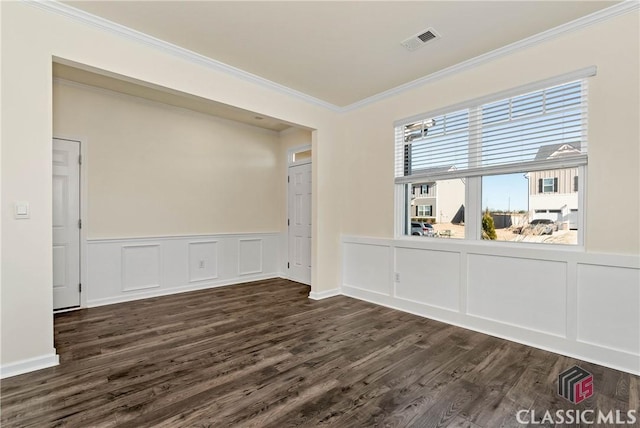 unfurnished room with dark wood-style floors, crown molding, wainscoting, visible vents, and a decorative wall