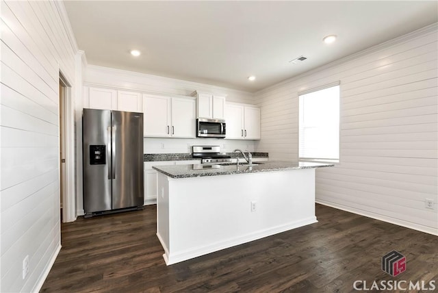 kitchen with an island with sink, dark stone countertops, a sink, crown molding, and appliances with stainless steel finishes