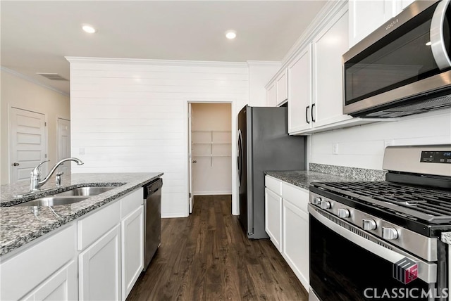 kitchen with white cabinets, stainless steel appliances, a sink, stone counters, and crown molding