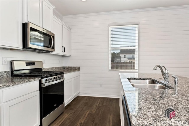 kitchen featuring stainless steel appliances, a sink, dark wood-style flooring, crown molding, and wooden walls