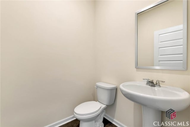 bathroom with baseboards, toilet, wood finished floors, and a sink
