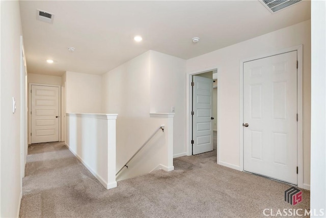 hall featuring baseboards, visible vents, carpet, and an upstairs landing