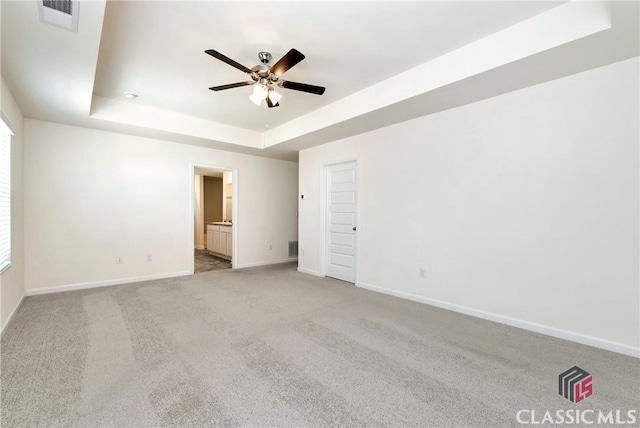 unfurnished bedroom featuring a raised ceiling, visible vents, carpet floors, ensuite bath, and baseboards