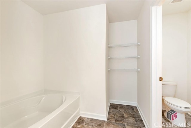full bathroom with a washtub, baseboards, stone finish flooring, toilet, and visible vents