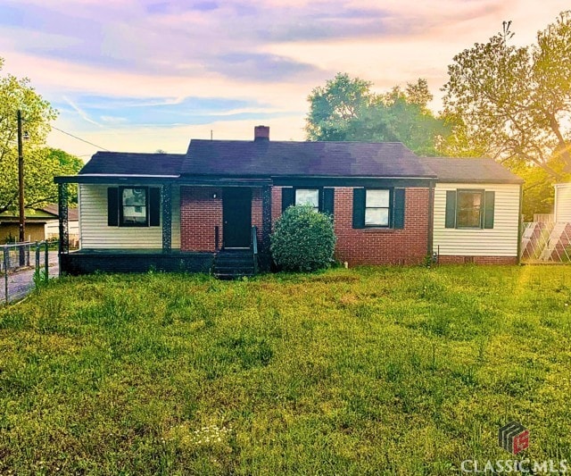 ranch-style house with a chimney, brick siding, fence, and a front yard