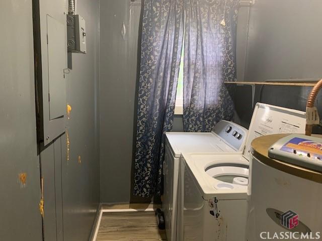 clothes washing area featuring water heater, laundry area, wood finished floors, and washer and clothes dryer