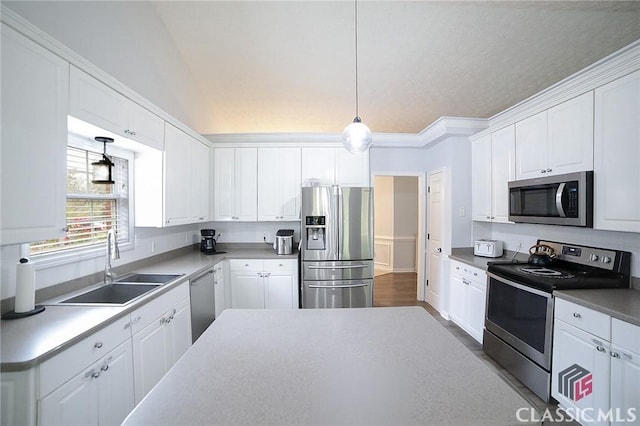 kitchen featuring appliances with stainless steel finishes, white cabinets, a sink, pendant lighting, and crown molding