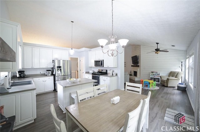 dining area featuring dark wood-type flooring, wooden walls, vaulted ceiling, and ceiling fan with notable chandelier