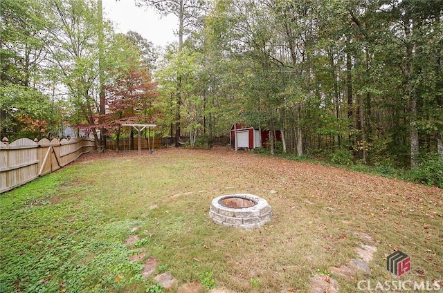 view of yard with fence, a fire pit, a shed, and an outbuilding