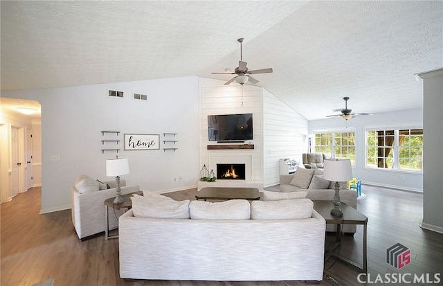 living room featuring lofted ceiling, a fireplace, a ceiling fan, a textured ceiling, and dark wood-type flooring