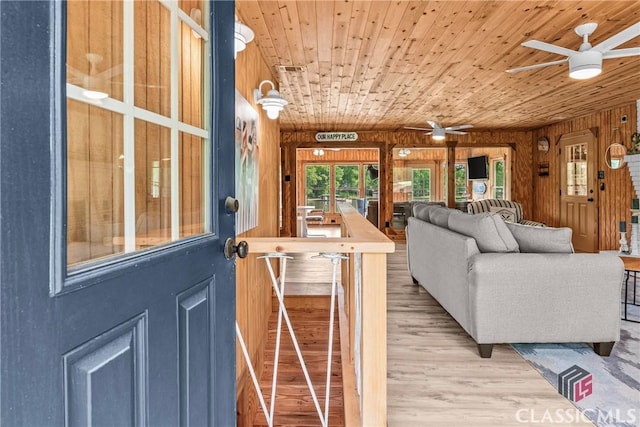 living room with wooden walls, wood ceiling, ceiling fan, and wood finished floors