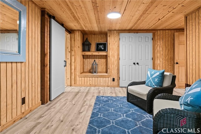 sitting room with wooden walls, baseboards, wooden ceiling, and light wood finished floors