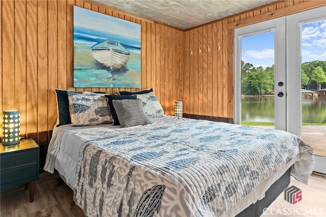 bedroom with french doors, access to exterior, wood finished floors, wooden walls, and a water view