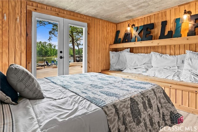 bedroom featuring french doors, wood walls, access to exterior, and wood finished floors