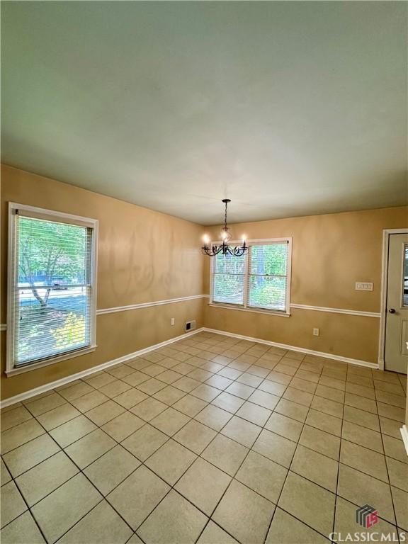 empty room with light tile patterned floors, baseboards, visible vents, and a notable chandelier