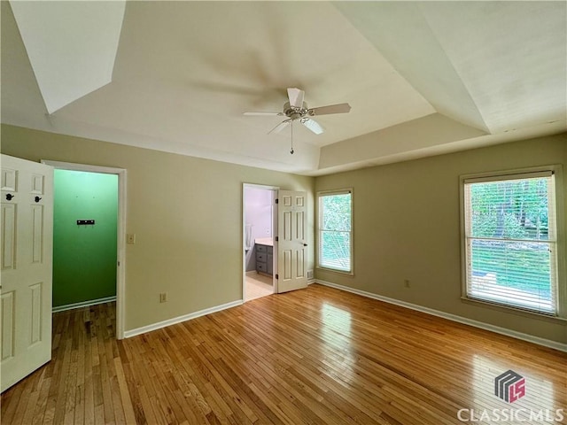 unfurnished bedroom with baseboards, a spacious closet, ensuite bathroom, and light wood finished floors