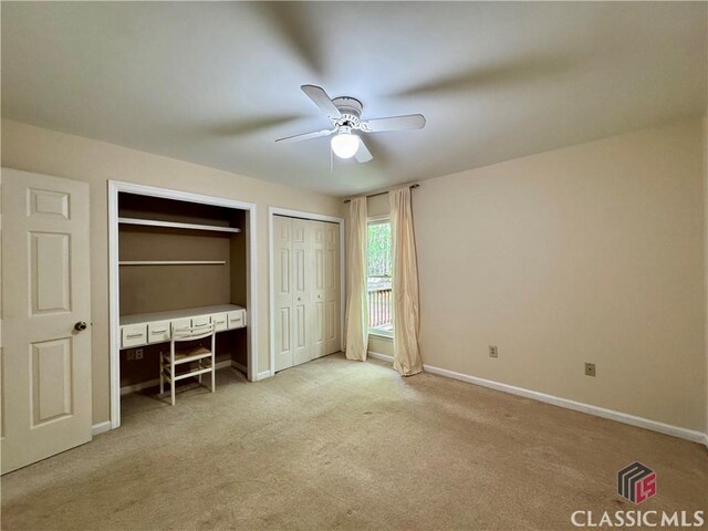 unfurnished bedroom with a ceiling fan, multiple closets, baseboards, built in desk, and carpet flooring