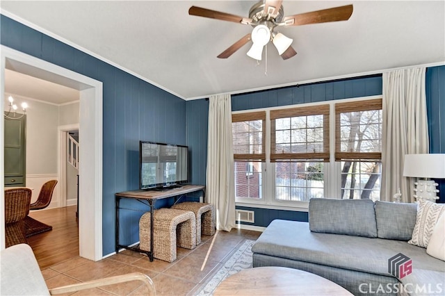 living room featuring tile patterned floors, ornamental molding, baseboards, and ceiling fan with notable chandelier