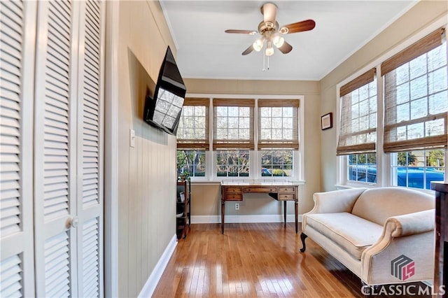 living area featuring crown molding, ceiling fan, built in study area, baseboards, and hardwood / wood-style flooring