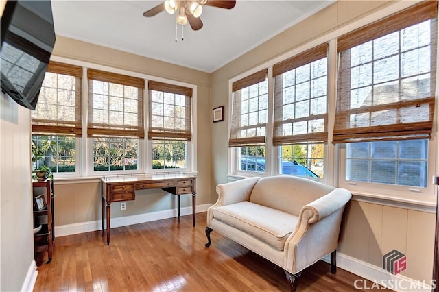 living area featuring wood-type flooring, crown molding, baseboards, ceiling fan, and built in desk