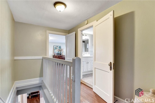 hall with a sink, wood finished floors, and an upstairs landing