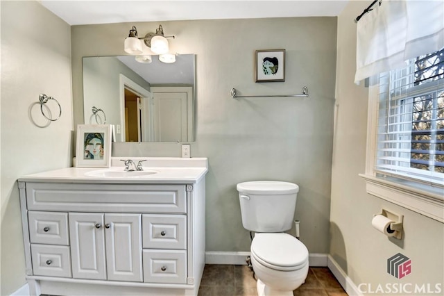 half bathroom with vanity, baseboards, tile patterned floors, and toilet