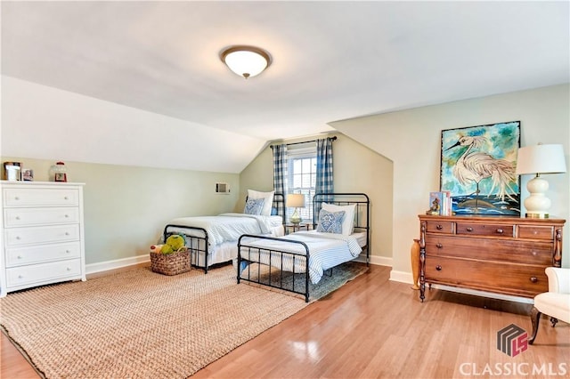 bedroom with baseboards, vaulted ceiling, and wood finished floors