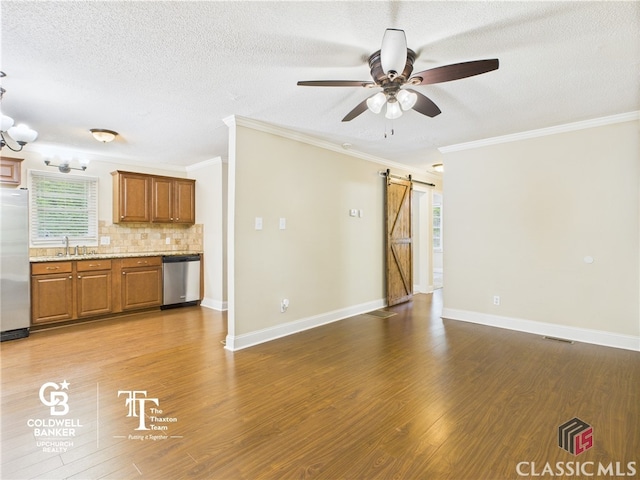 unfurnished living room with a barn door, a sink, ceiling fan, and ornamental molding