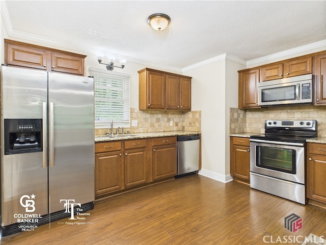 kitchen with decorative backsplash, crown molding, appliances with stainless steel finishes, a sink, and dark wood-style floors