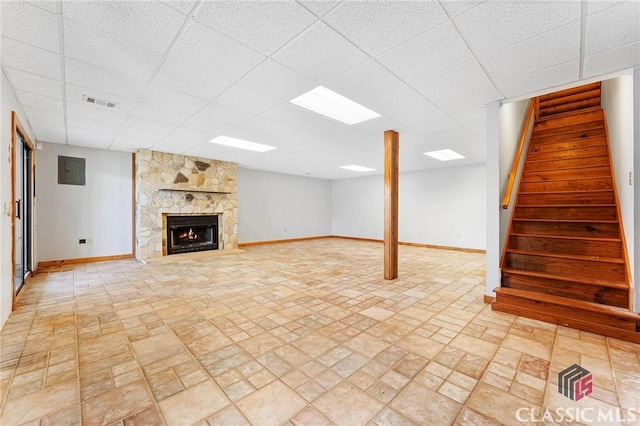 finished basement featuring a stone fireplace, baseboards, a drop ceiling, and stairway