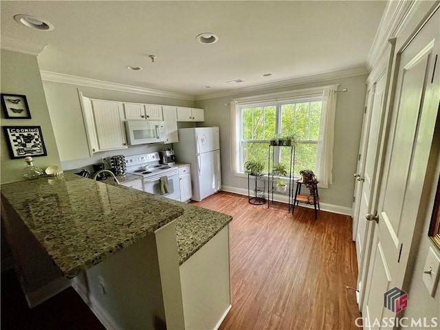 kitchen featuring a peninsula, wood finished floors, white appliances, white cabinetry, and dark stone countertops