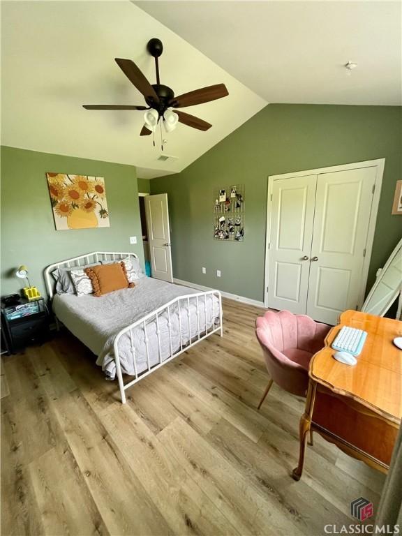 bedroom with a closet, wood finished floors, baseboards, a ceiling fan, and vaulted ceiling