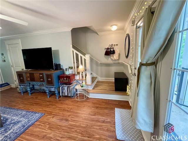 living area featuring crown molding, baseboards, wood finished floors, and stairway