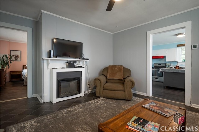living room featuring dark tile patterned floors, ceiling fan, baseboards, a glass covered fireplace, and ornamental molding