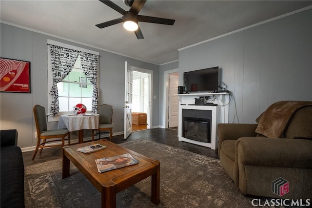 living area with crown molding, dark tile patterned floors, a ceiling fan, and a glass covered fireplace