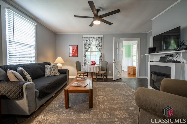 tiled living area featuring crown molding, a ceiling fan, baseboards, and a glass covered fireplace