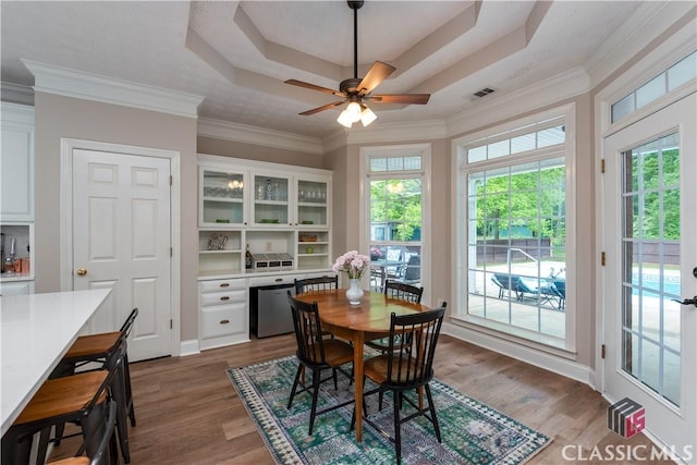 dining space with a ceiling fan, a tray ceiling, visible vents, and wood finished floors