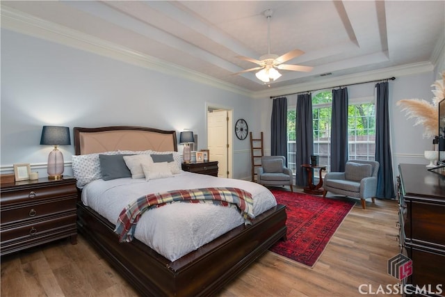 bedroom with visible vents, ornamental molding, a raised ceiling, and wood finished floors
