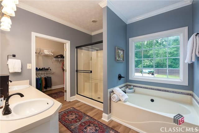 bathroom featuring a bath, a shower stall, wood finished floors, a sink, and ornamental molding