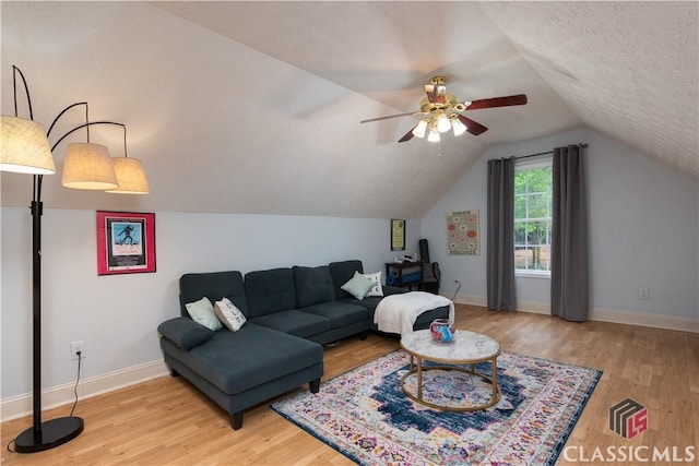 living area featuring a ceiling fan, a textured ceiling, vaulted ceiling, light wood-type flooring, and baseboards